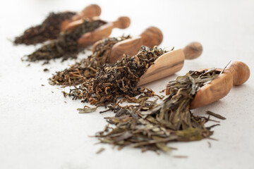 A view of several wood scoops of loose leaf tea spilling out onto a white background.