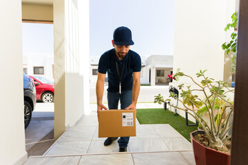 Delivery man in uniform carefully drops off a package at a house entrance, showcasing the...