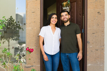 New Hispanic couple poses for a photo at the entrance of their new home