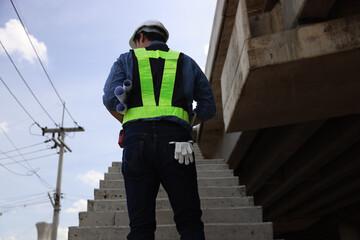 A smart Asian male engineer standing on a staircase concrete viaduct with an unfinished railway...