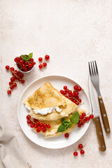 Crepes or thin pancakes with cheese cottage or curd and fresh red currant berries, top view