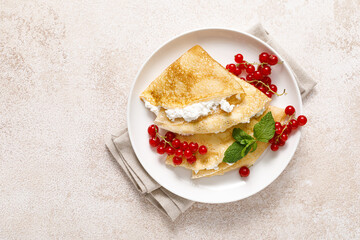 Crepes or thin pancakes with cheese cottage or curd and fresh red currant berries, top view