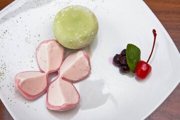 Mochi ice, strawberry and green tea mochi ice accompanied by cherry and blueberries on wooden table