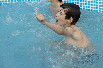 A boy with wet hair is enthusiastically swimming in a pool, giving a thumbs-up gesture. Another...