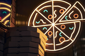 The pizza symbol is made of LED lamps. Round pizzeria signs next to pizza boxes with a place to copy. The concept of pizza delivery at home. High quality photo