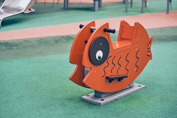 A swing in the form of a fish on the playground in the park. Covering for sports and playgrounds. Rubber mulch for safety and injury prevention. With space to copy. High quality photo