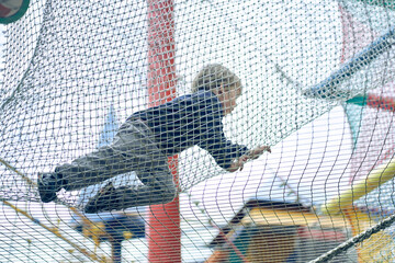 A joyful boy is playing in a children's maze, jumping on a grid. Hobbies and entertainment. Happy...