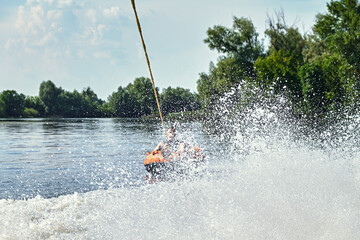 Person being towed on an inflatable tube across a lake, with water splashing dramatically in the...