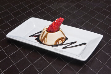 panna cotta dessert with strawberry and garnished with chocolate syrup on black background, food