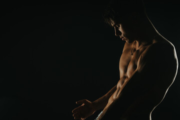 Shirtless muscular young man posing in low light, showcasing his defined physique and strength....
