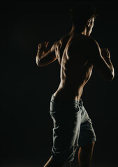 Fototapeta premium Muscular man performing shadow boxing in a dimly lit setting. The image captures the strength, fitness, and determination of the individual.