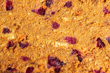Close-up of a textured baked food surface with visible chunks of dried plums and other ingredients. The golden-brown crust showcases a delicious blend of natural ingredients. Organic texture.