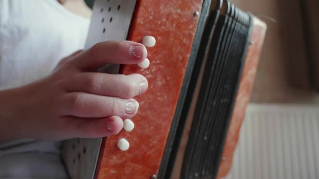 Little girl playing a vintage harmonica buttons with her fingers in a room, closeup shot.