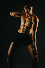 Naklejka premium Fit man displaying his toned abs in a dramatic light setting, focusing on his athletic body and fitness.