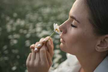A woman is holding a flower and smelling it. Concept of peace and tranquility, as the woman takes a moment to appreciate the beauty of the flower.