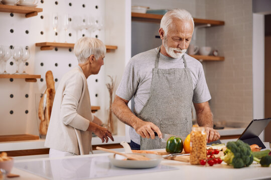 a happy senior couple preparing a healthy meal together, using a tablet