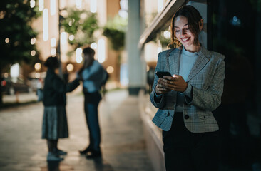 Young woman smiling and texting on her smart phone at night in an urban environment. A blurred...