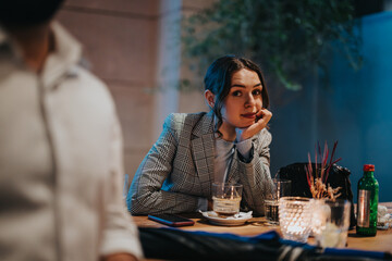 Young woman in casual attire sitting at a restaurant or bar, enjoying a drink. Cozy, intimate setting with candles and drinks on the table.