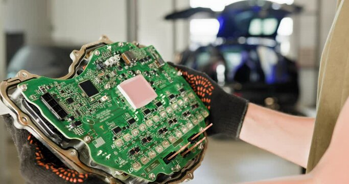 Auto mechanic holding the ECU of a modern electric car in a workshop. Close-up view of the circuit board. Car repair and maintenance. Mechanic Repairing Electric Car Engine with Voltmeter in Workshop