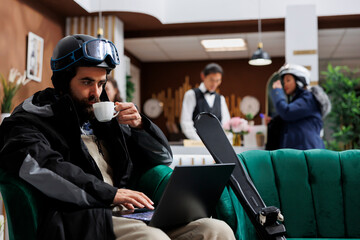 Within lavish hotel foyer, gentleman in snow clothing sips coffee, engrossed in digital device,...
