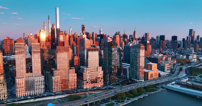 New York buildings are lit with pink light of sunset. Drone rises above the East River revealing view on the cityscape.