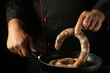 The cook puts the sausage in the frying pan with his hand. Cooking or frying sausage in the kitchen at home