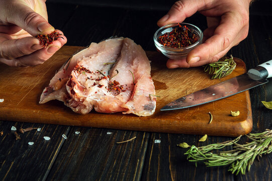 The cook adds dry aromatic spices to fresh fish fillet with his hands. The concept of cooking a fish dish according to an old recipe.