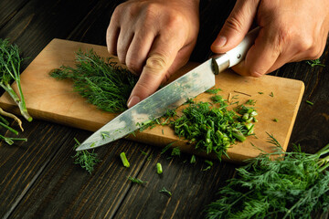 Chopping dill with a knife into a man hand to add to food before preparing a vegetarian dinner.