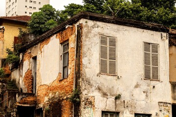 Casa velha com paredes descascadas e janelas de madeira quebradas. 