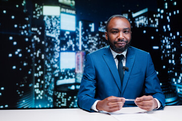 News presenter on live night show transmitting latest information, broadcasting reportage for television content. African american media journalist reading daily headlines in newsroom.