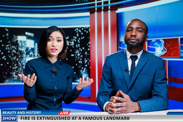 Newscasters announcing fire hazard at famous landmark, firefighters stopping flames from destroying history and beauty. Presenters team doing television reportage on night show live.