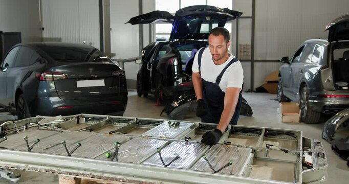Arabian Male Technician Engages With An EV Car Battery Cell Module, Troubleshooting And Examining It In A Modern Vehicle Repair Shop. EV Car Battery In Workshop. Auto Service, Electric Car Battery.