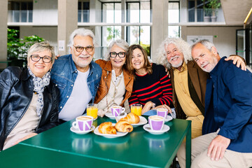 Portrait of happy senior group of pensioner friends smiling at camera while having breakfast together at cafeteria bar. Elderly lifestyle concept.