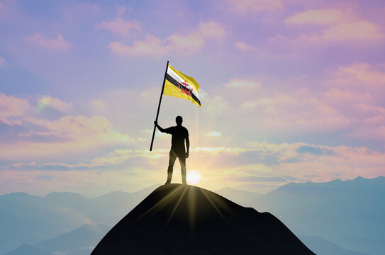 Waving flag of Brunei at the top of a mountain summit against sunset or sunrise. Brunei flag for Independence Day.