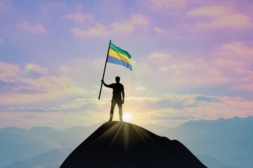 Waving flag of Gabon at the top of a mountain summit against sunset or sunrise. Gabon flag for Independence Day.