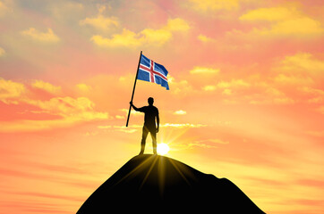 Waving flag of Iceland at the top of a mountain summit against sunset or sunrise. Iceland flag for Independence Day.