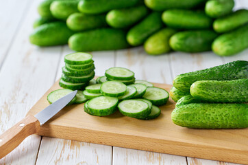 Whole and sliced cucumbers on a cutting board on a wooden table, selective focus.