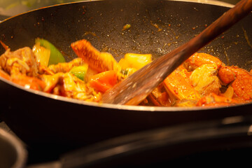 Motion blur image wooden spoon stirs a pot of food in a black pan. The food appears to be a mix of vegetables and meat, and it looks delicious. Scene is warm and inviting