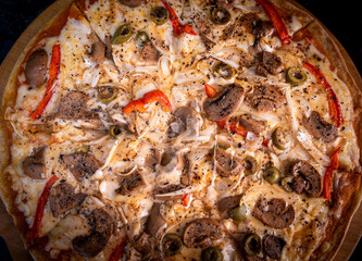 Close-up of a hand taking a slice of vegetarian pizza with onions, bell pepper, and vegetables on a wooden board.