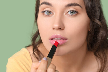 Beautiful young woman applying red lipstick on green background, closeup