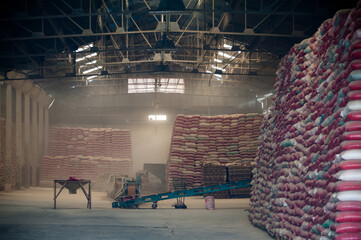 Grain packing warehouse with conveyor belts moving product into sacks. Pallets of sacks stacked ready for shipping. Dity air creates a moody backdrop