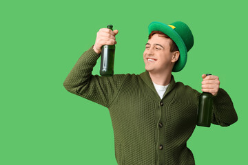 Happy young man in leprechaun's hat with bottles of beer on green background. St. Patrick's Day...
