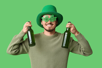 Happy young man in leprechaun's hat with party glasses and bottles of beer on green background. St....