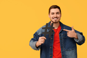 Handsome young man pointing at hashtag sign on yellow background