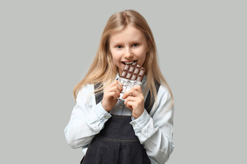 Cute little girl eating sweet chocolate bar on grey background