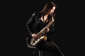 Naklejka premium Beautiful young woman playing saxophone on dark background