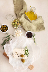 Paper with tasty feta cheese, olives, rosemary and peppercorn on white background
