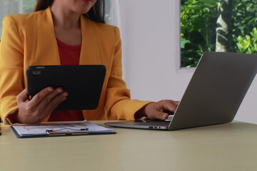 A middle-aged businesswoman in a yellow suit works at a desk on tips for financial stability. She plans expenditures to match her income.