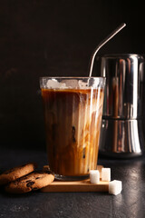 Glass of iced latte with sweet cookies and cubes of sugar on black background