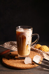 Glass cup of iced latte with coffee beans and sweet cookies on wooden table